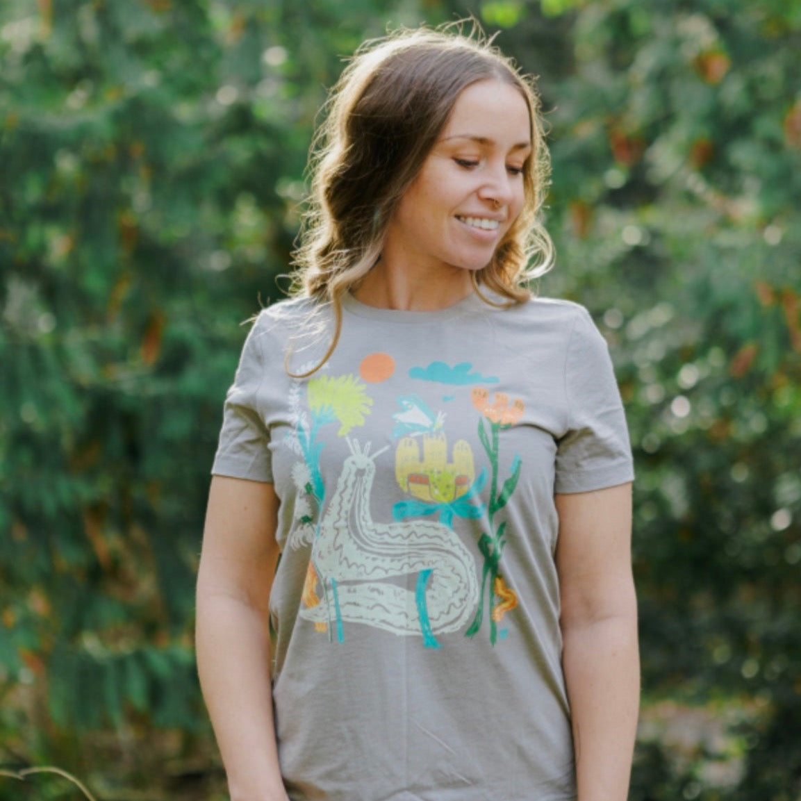 Woman wearing light brown t shirt with colorful print of plants and bugs