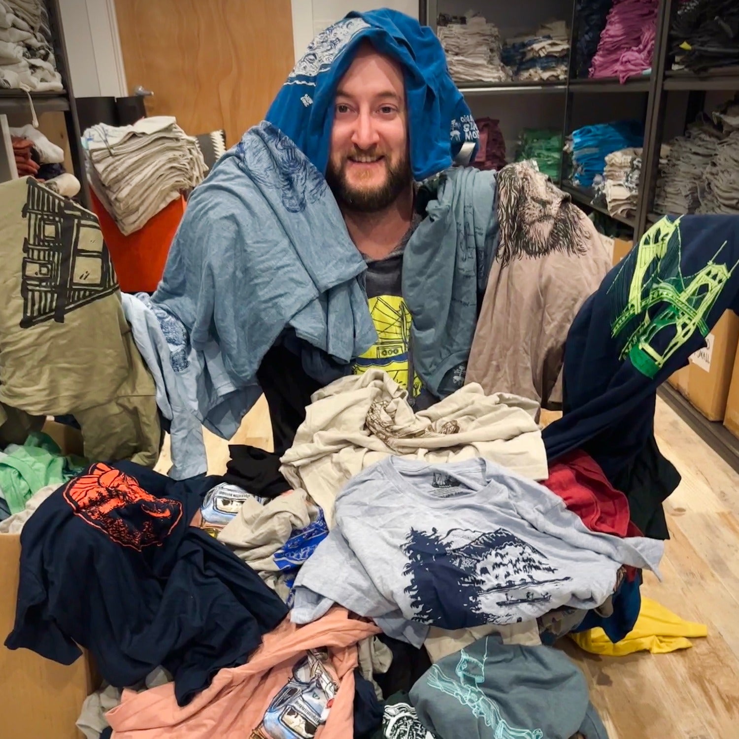 man in a pile of different colored t-shirts with different designs and colors of inks.