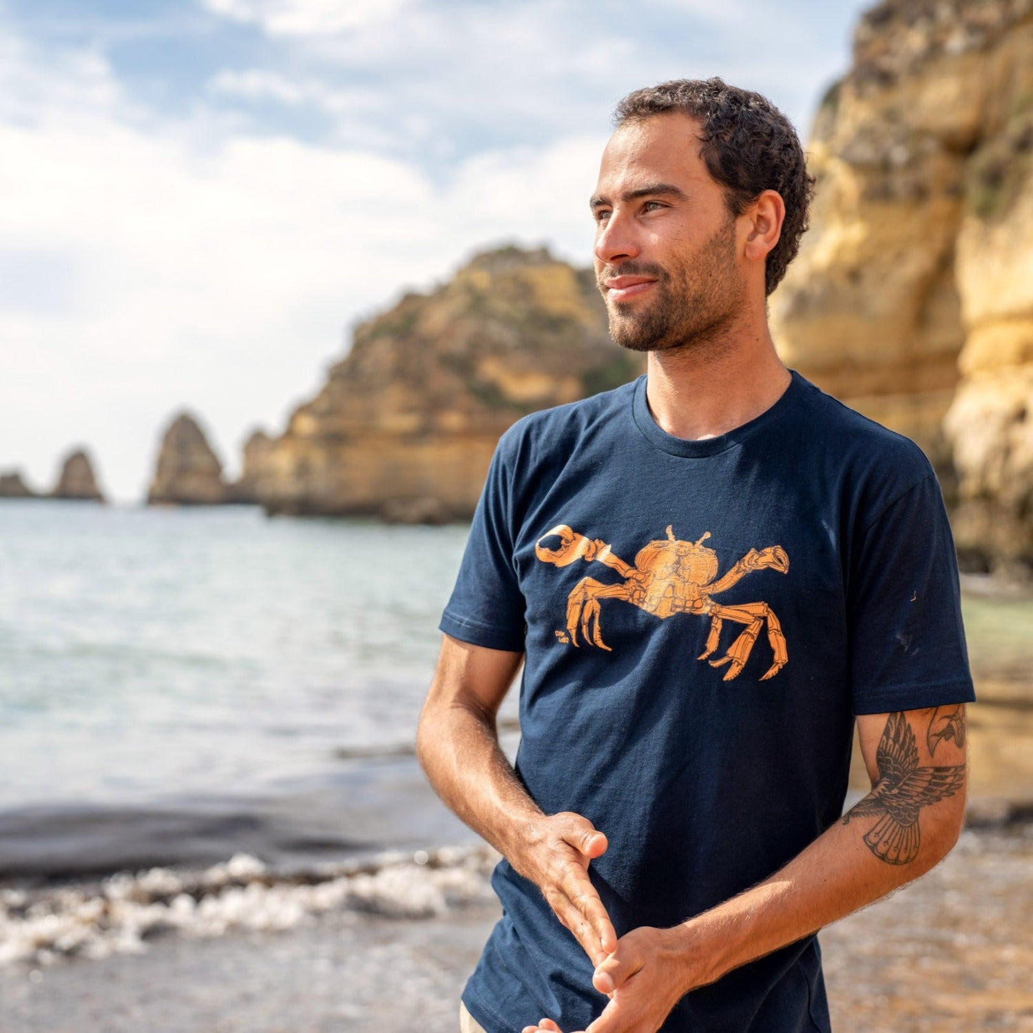 Man on the beach wearing a blue t-shirt with a crab on it. 