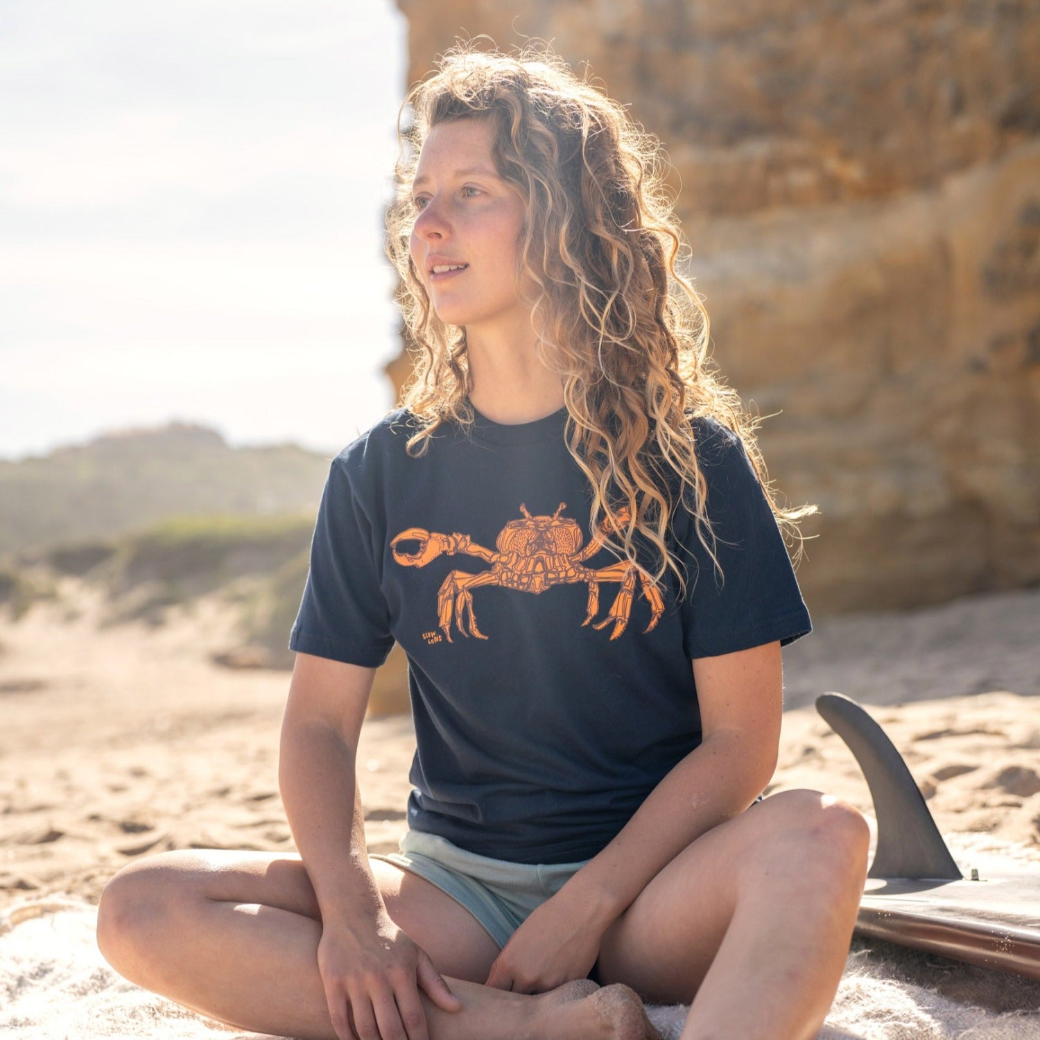 Girl on beach wearing blue t-shirt with a crab on it.
