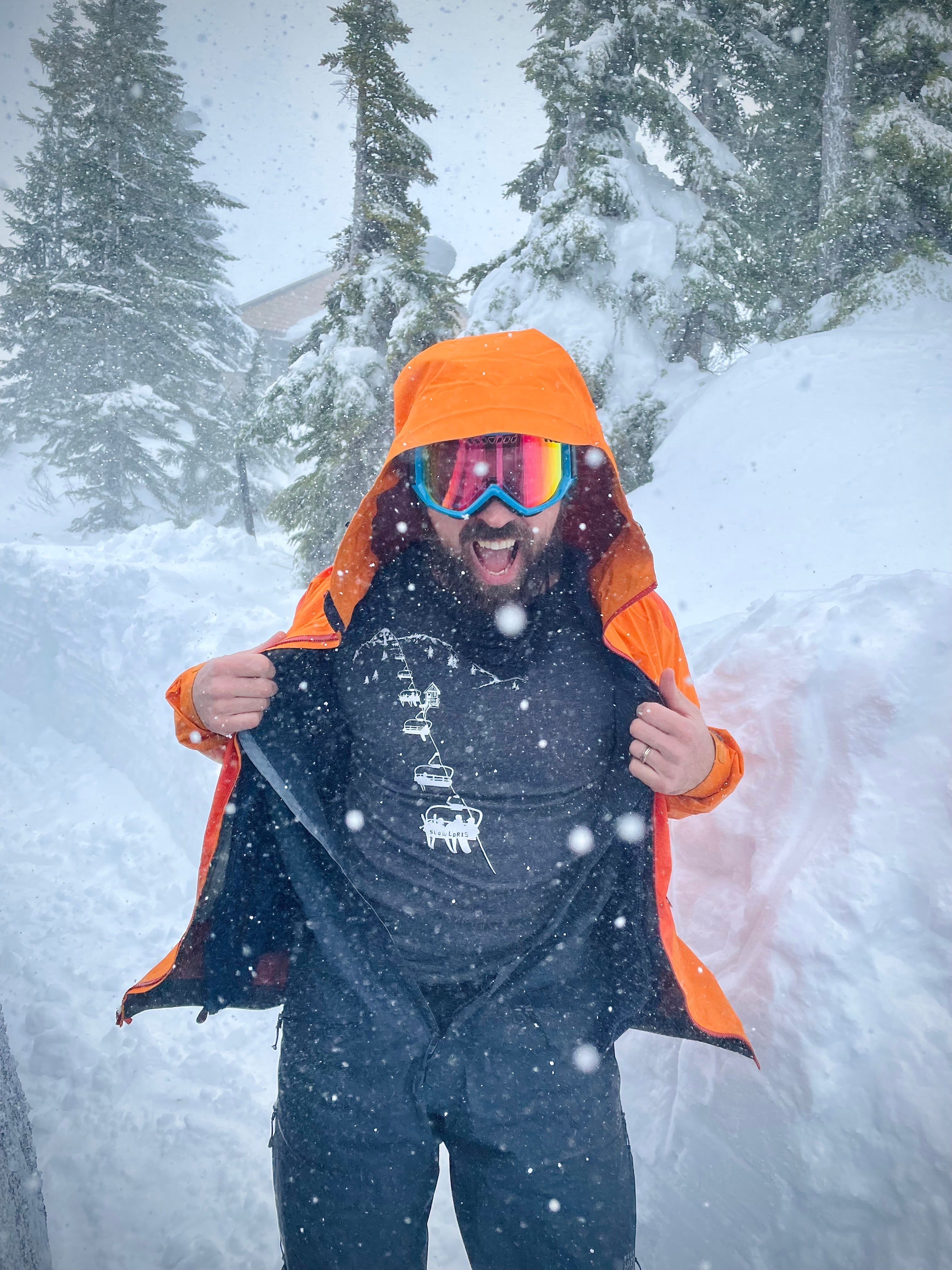 Smiling man in snowstorm, opening snowsuit to reveal t shirt printed with chairlift.