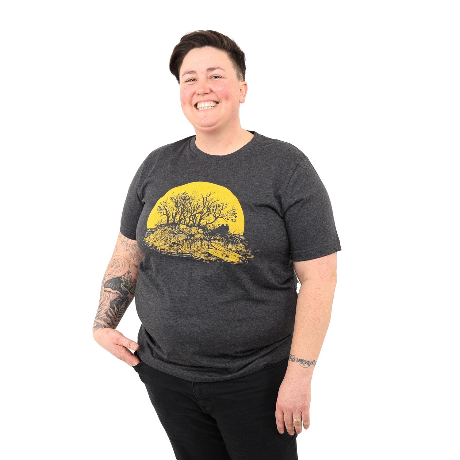nice smiley woman with one hand in her pocket while wearing black jeans and a dark gray t-shirt with yellow kayaker print.