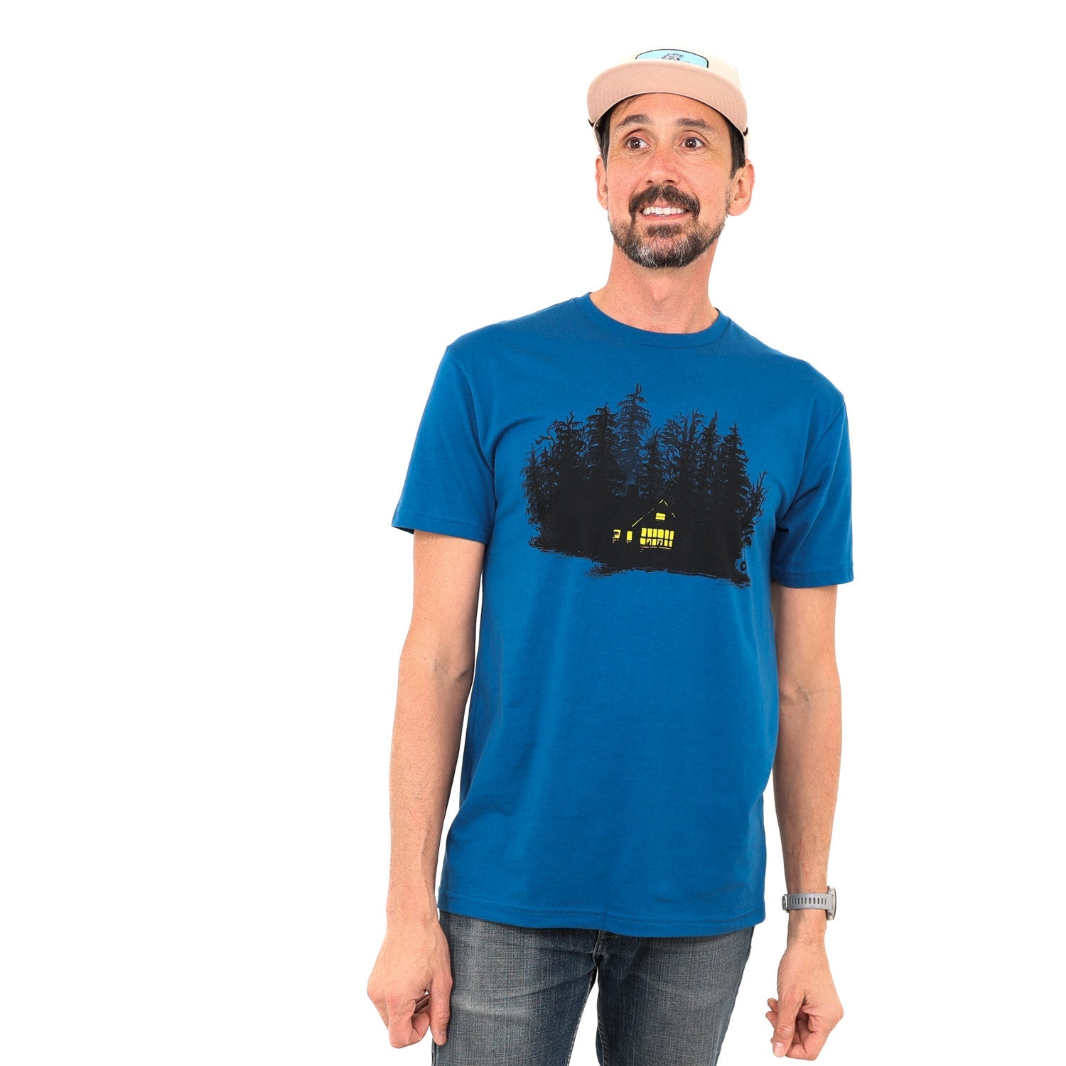 Man wearing blue t-shirt with print of black ink of silhouetted trees with yellow ink house lights shining out of darkness. Two animals sitting in the window.