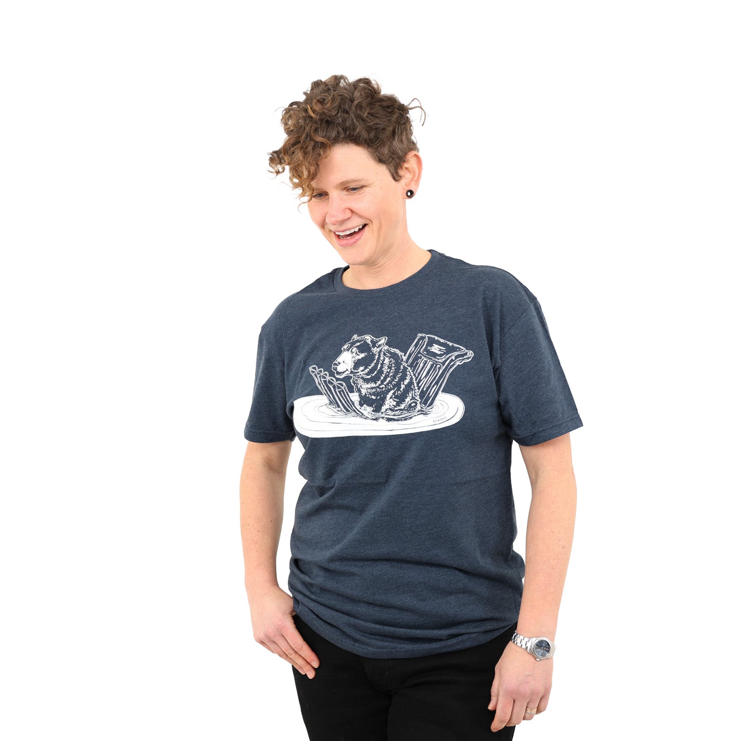 Woman with short curly hair wearing a blue t shirt screen printed with a bear sitting on a floatie in the water. 