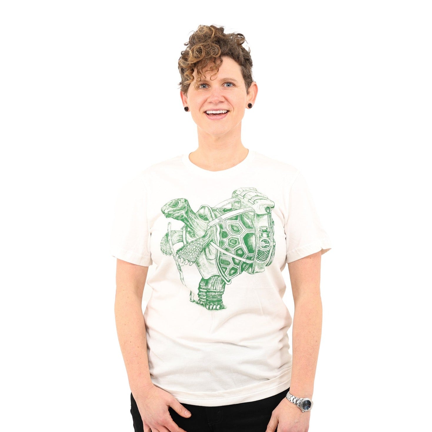 Woman in white background. wearing white shirt with green ink of a hiking tortoise. 