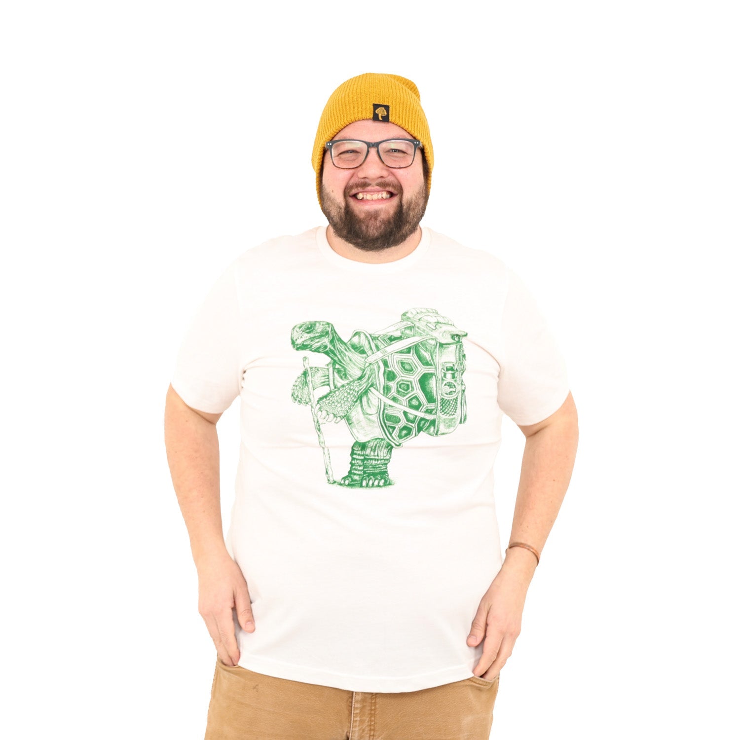 Friendly guy smiling wearing glasses and a mustard colored beanie. Also wearing white shirt with hiking tortoise in green ink