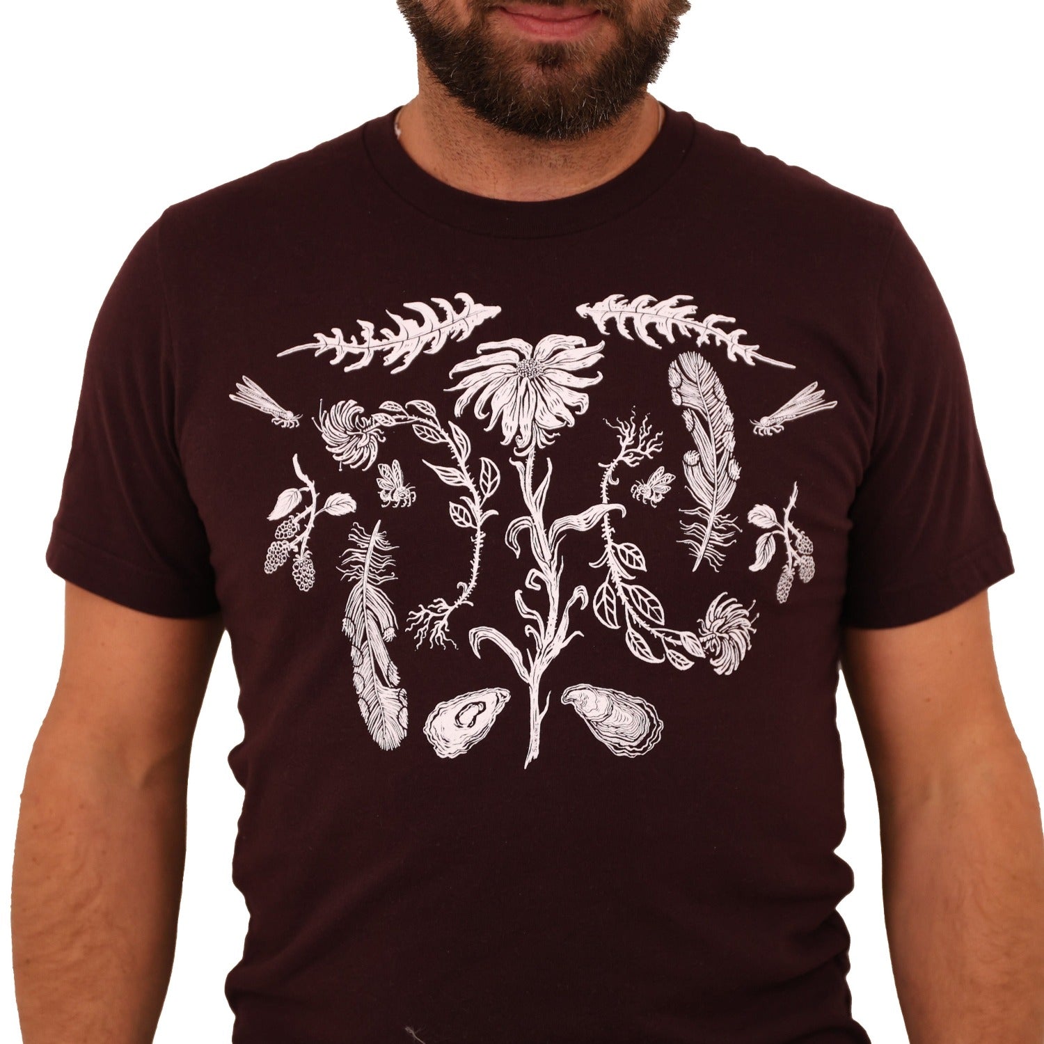 Man wearing a oxblood colored t-shirt with white ink of flowers, ferns, feathers, shells, etc