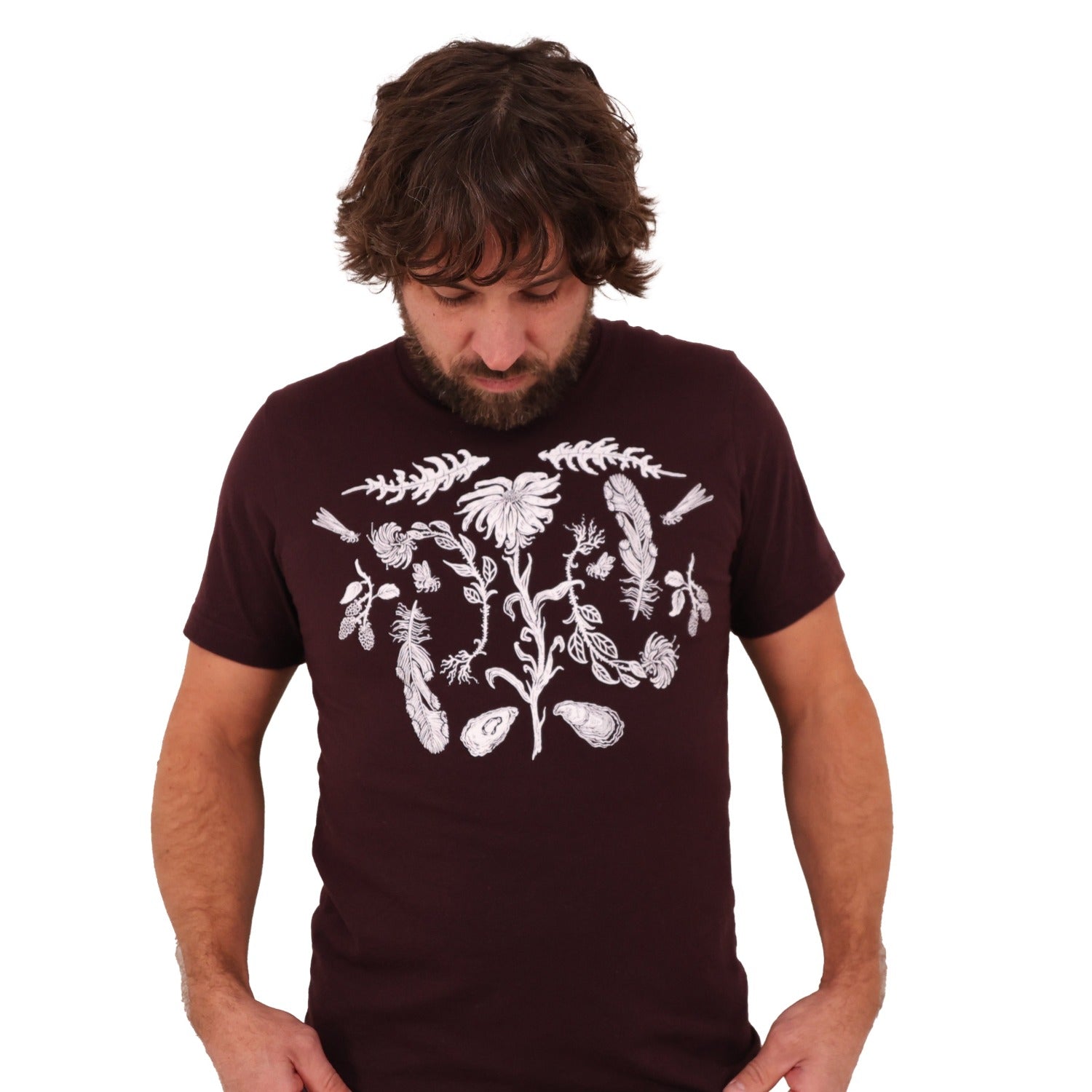 Man wearing a oxblood colored t-shirt with white ink of flowers, ferns, feathers, shells, etc