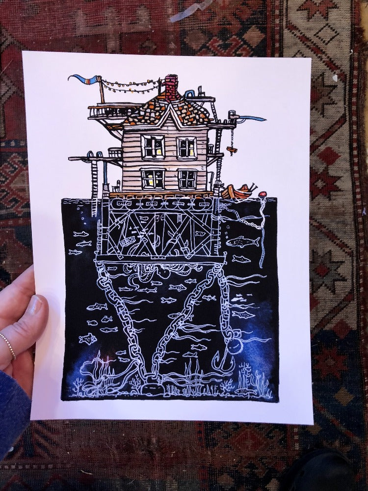 hand holding art print painting of a colorful cartoon 3 story house underwater scene.