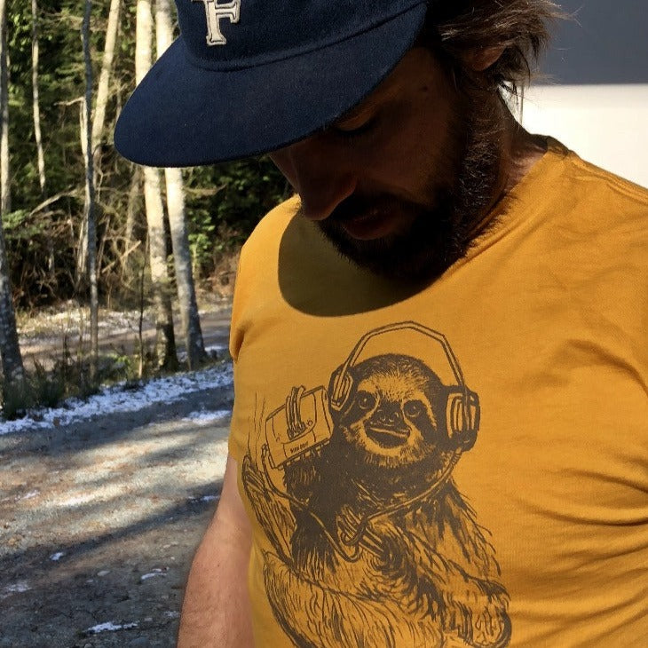 Man wearing a mustard yellow shirt with a brown screen print of a sloth listening to music on headphones.