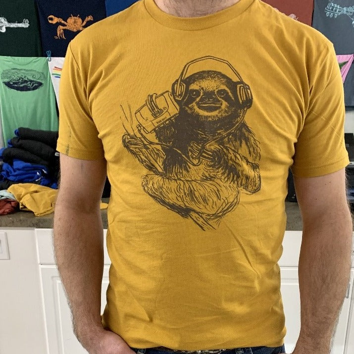 close up of man wearing a mustard yellow shirt with a brown screen print of a sloth listening to music on headphones.