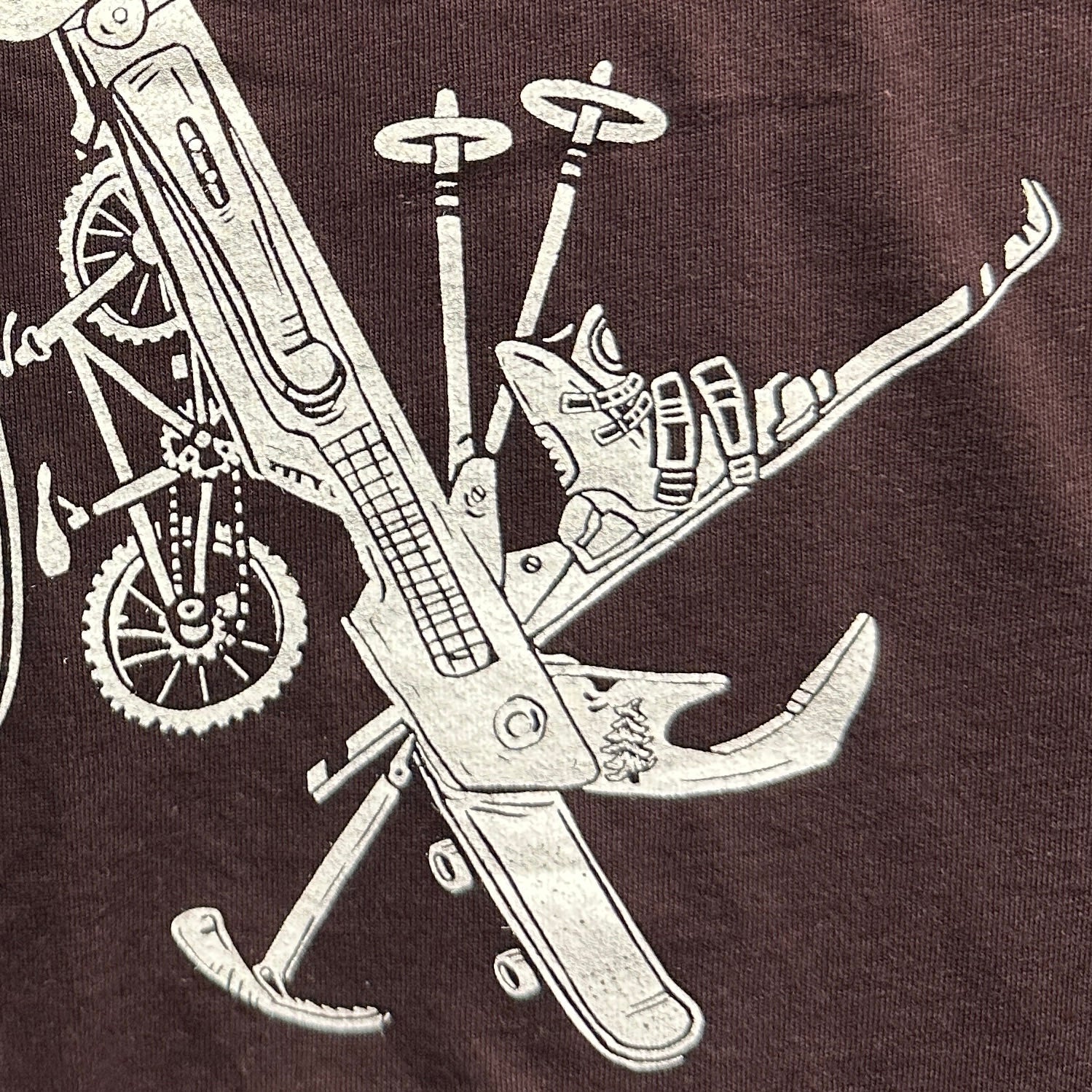 oxblood colored t-shirt with a white print of a multitool. The tools within the multitool are actually adventuring items- kayak, fishing pole, skis, ice axe, etc etc.