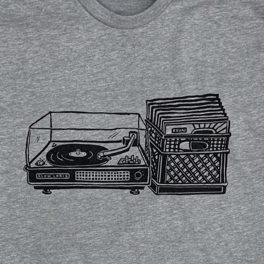 Close up of light grey shirt with black print of a record player with a milk crate full of records next to it. 