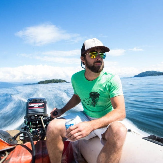 man driving inflatable skiff while wearing a green t-shirt with a black jelly fish print on it. Water, islands, blue sky, and clouds in the background