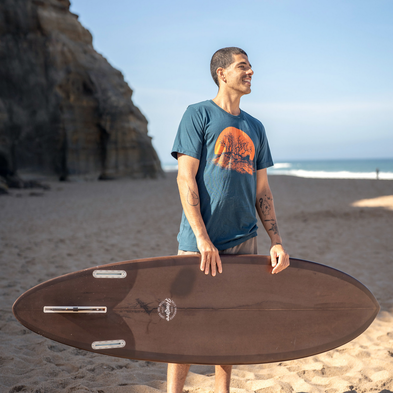 Man on beach holding surf board while wearing a kayaker t-shirt