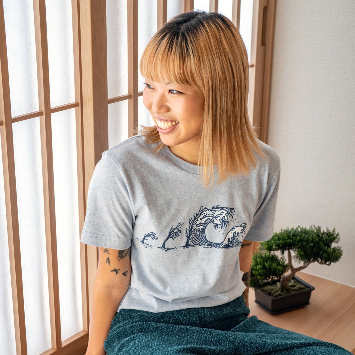 Girl looking to the side while wearing light blue tee with trees turning to waves across the chest.