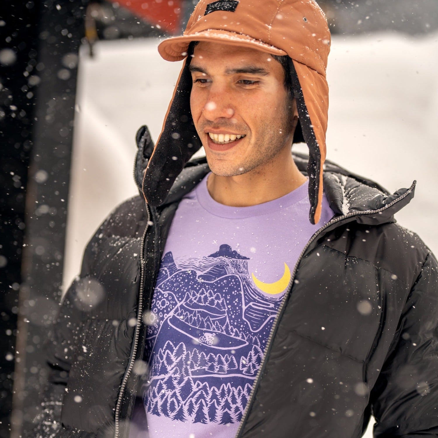 man in the snow wearing a hat and jacket. Slow Loris Night Ride T-Shirt is shown through open coat