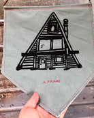 Green canvas pennant printed with black A-Frame house design, held in a hand.