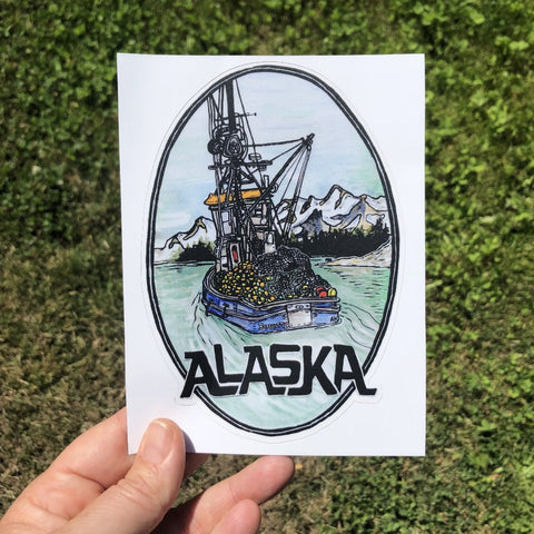 Colorful sticker of fishing boat with Alaska written underneath, held in hand.