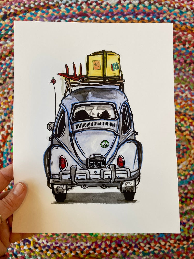 Hand holding a colorful art print of a VW bug from the rear, with silhouettes of a long-haired person in the driver's seat and a dog in the passenger seat.