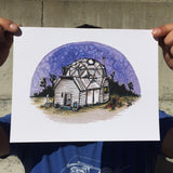 Colorful art print of a geodesic dome house in the desert, under a purple night sky. Watercolor and ink. Held by finger and thumb at the  corners to show size.