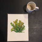 A print of a painting of bladderwrack seaweed, next to an empty coffee mug for scale.