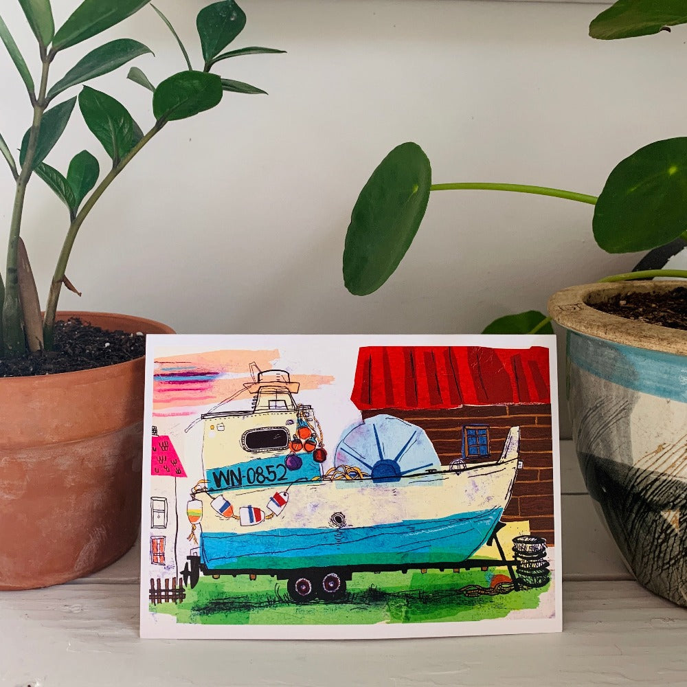 A greeting card printed with a colorful tissue-paper and ink painting of an old fishing boat in a yard.