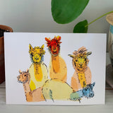 A greeting card, printed with a colorful tissue and ink painting of golden alpacas on the front.