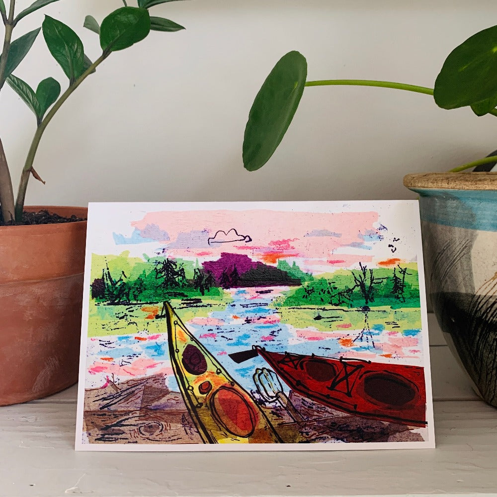 A greeting card featuring a colorful tissue and ink painting of kayaks on a beach.