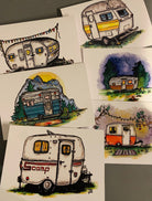 Set of six greeting cards, each printed with a different colorful painting of a vintage camper trailer, laid flat on a table.