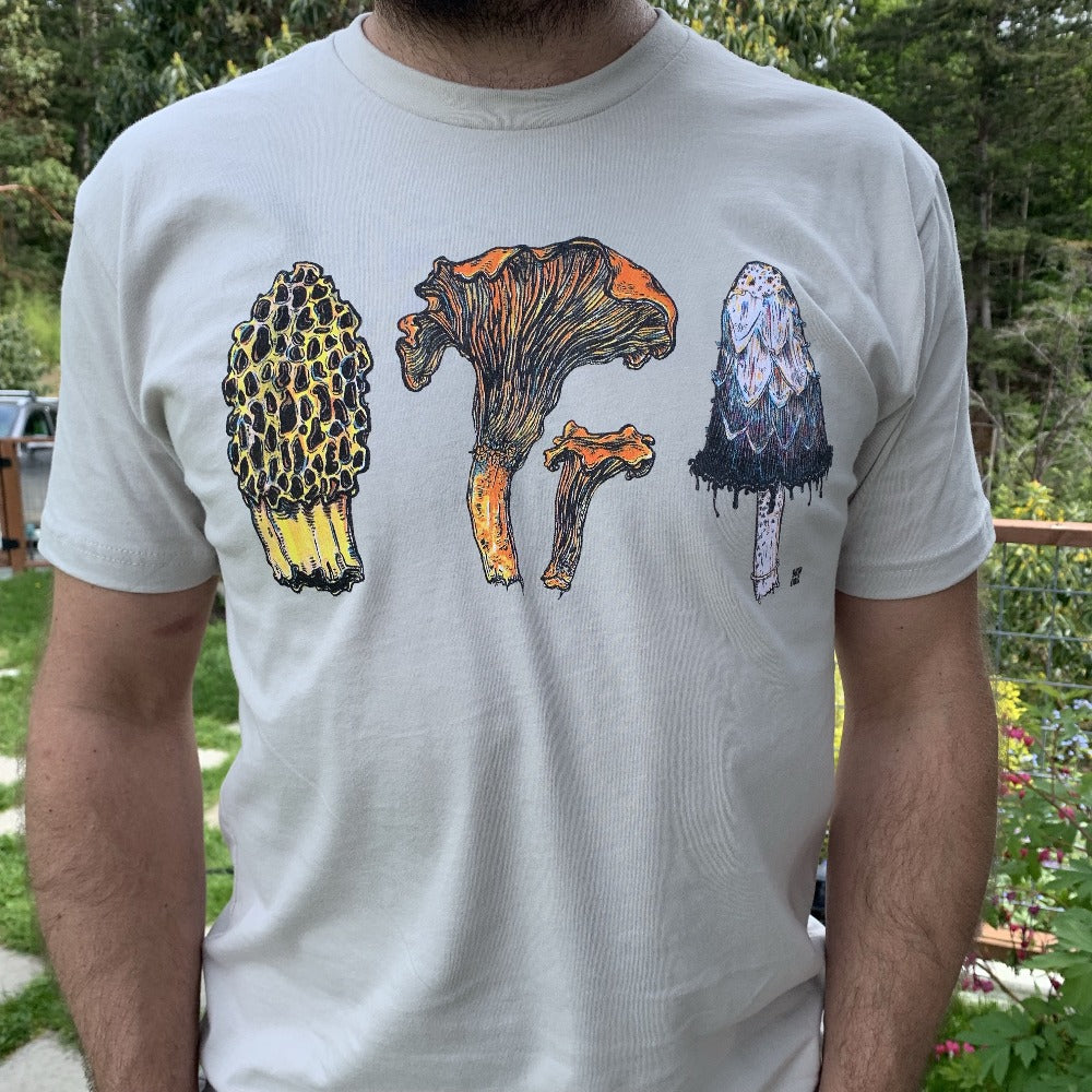 man wearing a tan colored shirt with three mushrooms- morel, chantrelle, and shaggy mane