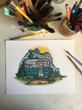 Original painting of a vintage Bell camper trailer in a mountainside camp. Painting is lying on a desk with brushes and pens.