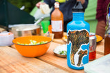 A colorful sticker of two chanterelle mushrooms, applied to a water bottle. The water bottle sits on a picnic table full of food.