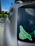 A car window adorned with our Dog Island sticker - a green dog's head in the shape of Guemes Island.