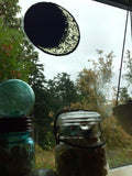 A large vinyl "stained glass" sticker in the shape of the waxing crescent moon, affixed to a window. Various glass jars are in the windowsill.