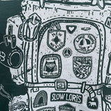 Close-up detail of a t shirt design: an old-school backpack covered with various badges - New Mexico, Lake Tahoe, Yosemite, plus many more. The design is printed in white ink on a green t shirt.