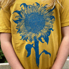 close up of a  mustard colored t-shirt with light blue print of an intricate sunflower.