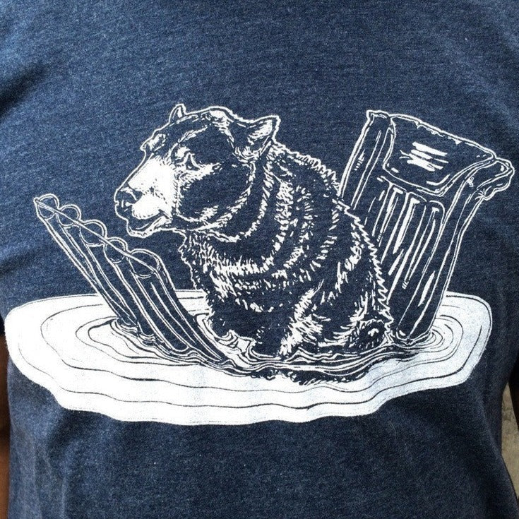 Close-up of blue t shirt with white print of a bear on a pool floatie. 