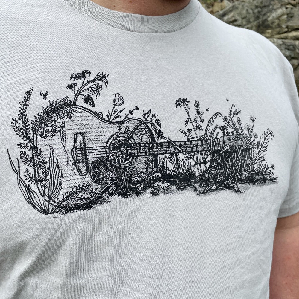 A drawing of a guitar on its side, overgrown with plants, printed in black ink on a light gray t shirt.