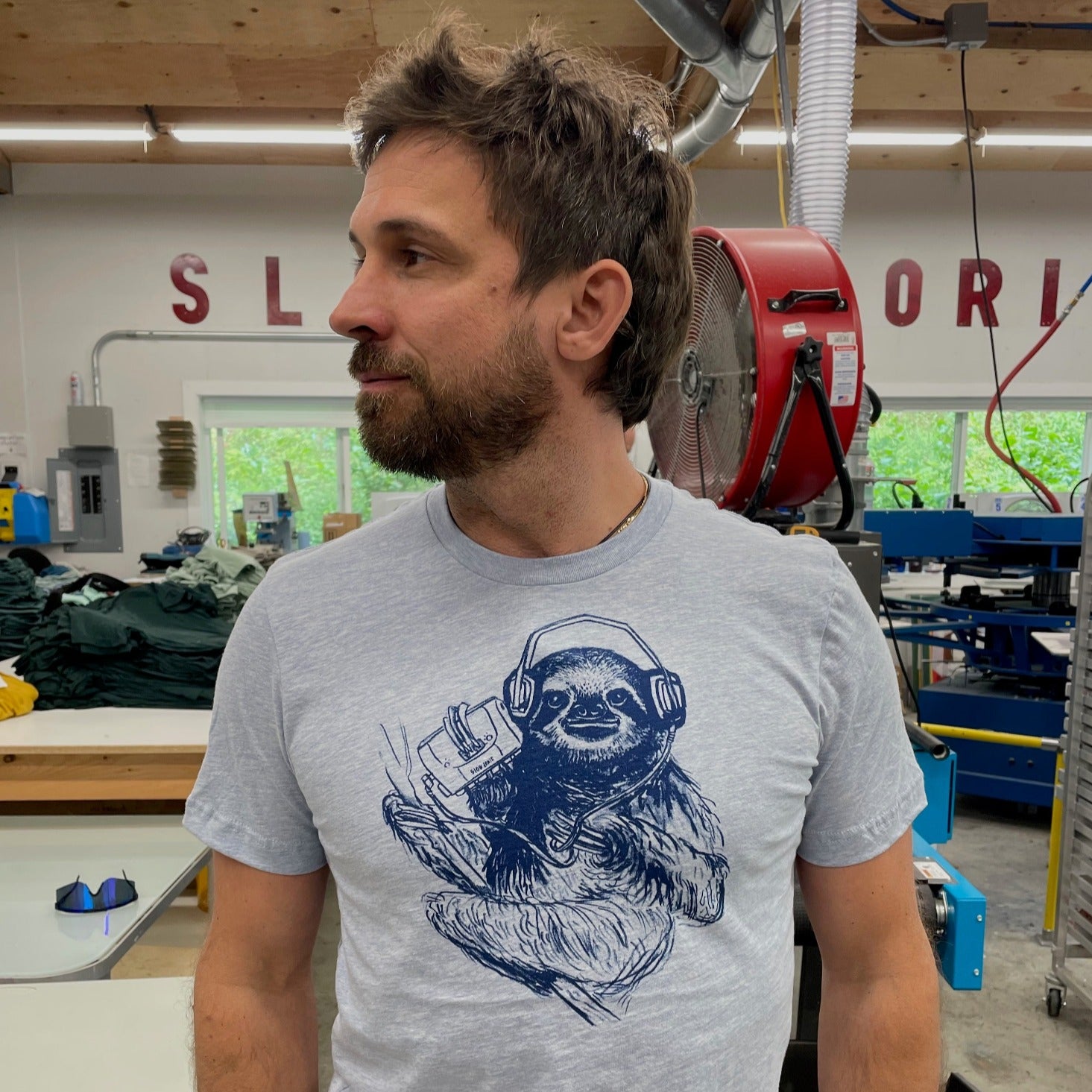 light blue shirt with dark blue screen print of a sloth listening to music on headphones.