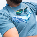 Close-up of t shirt printed with a blue whale, worn by a man with sunglasses around his neck.