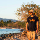 T shirt printed with an orange Dungeness crab, modeled by a man on a beach holding a fishing pole.