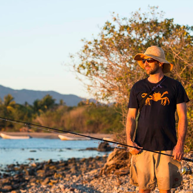 T shirt printed with an orange Dungeness crab, modeled by a man on a beach holding a fishing pole.