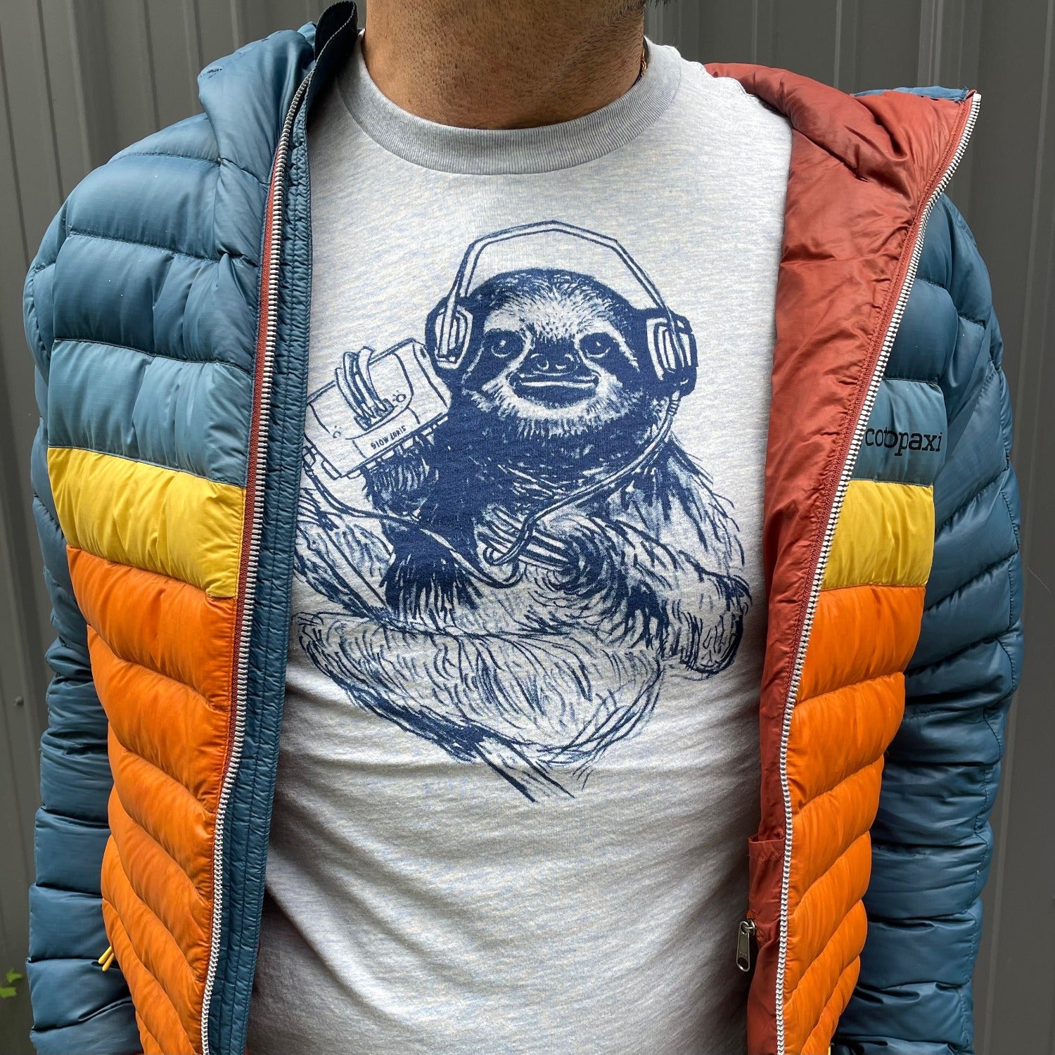 light blue shirt with dark blue screen print of a sloth listening to music on headphones.