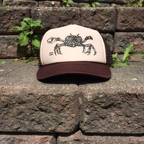 Brown and tan trucker hat printed with a Dungeness crab in black ink.