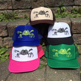 Stack of hats in a variety of colors, printed with a Dungeness crab line drawing.