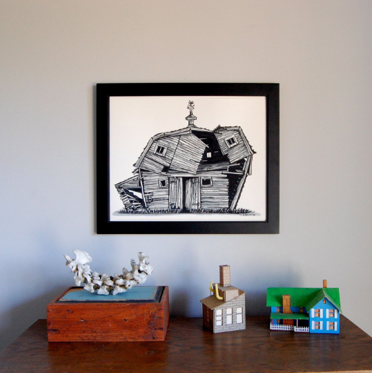 Framed black and white art print of  abandoned barn, hanging on wall above small table.